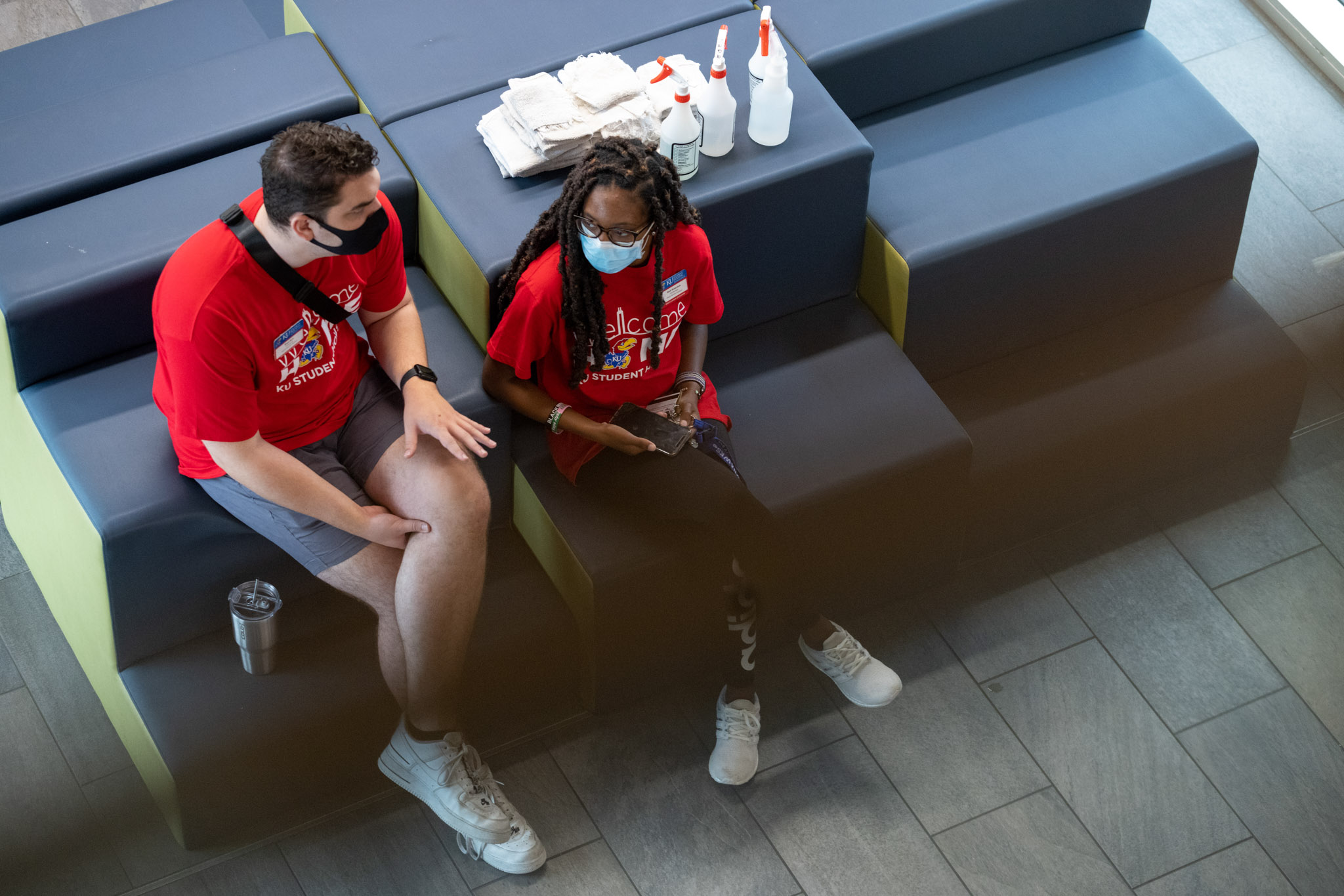two Student Housing student employees wearing face masks, conversing in the Daisy Hill Commons beside their cleaning supplies
