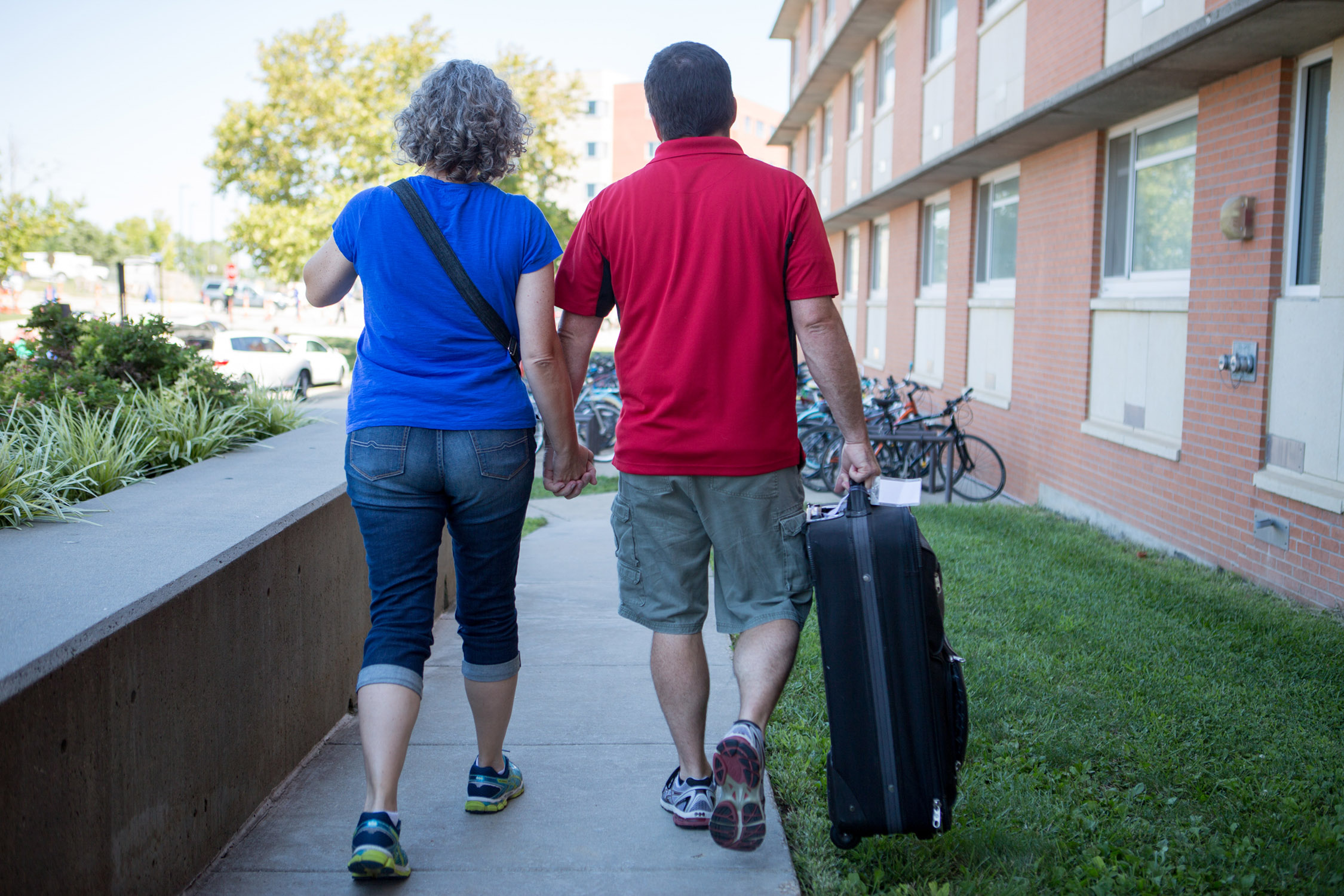 two parents in red and blue KU colored shirts, holding hands, walking away from Ellsworth Hall