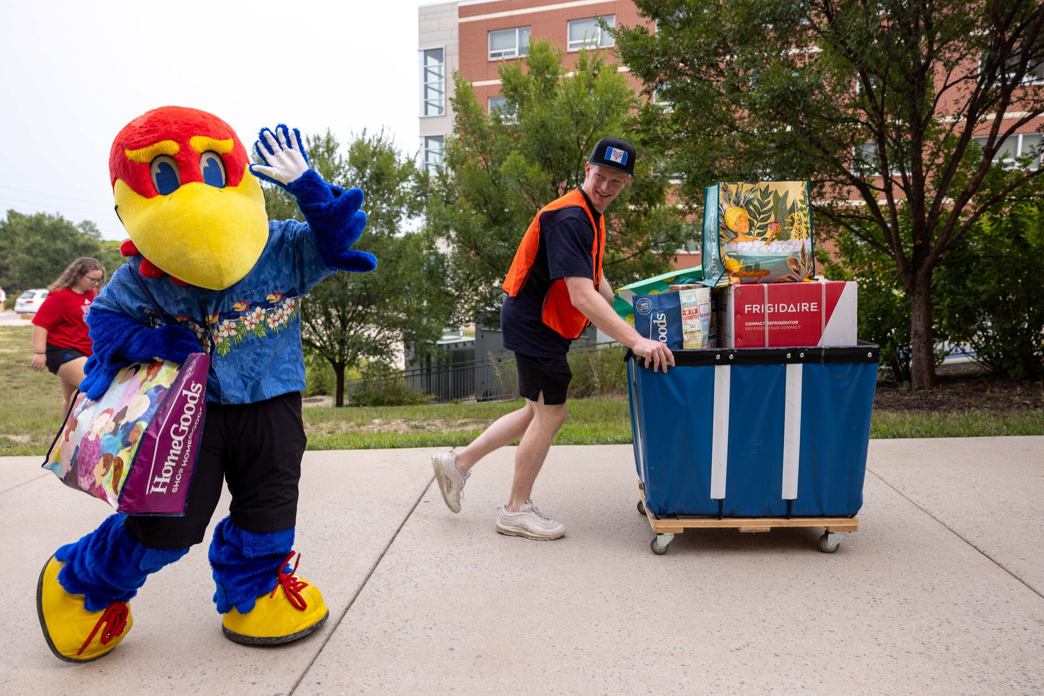 Baby Jay waving at the camera with a student pushing a move-in cart 