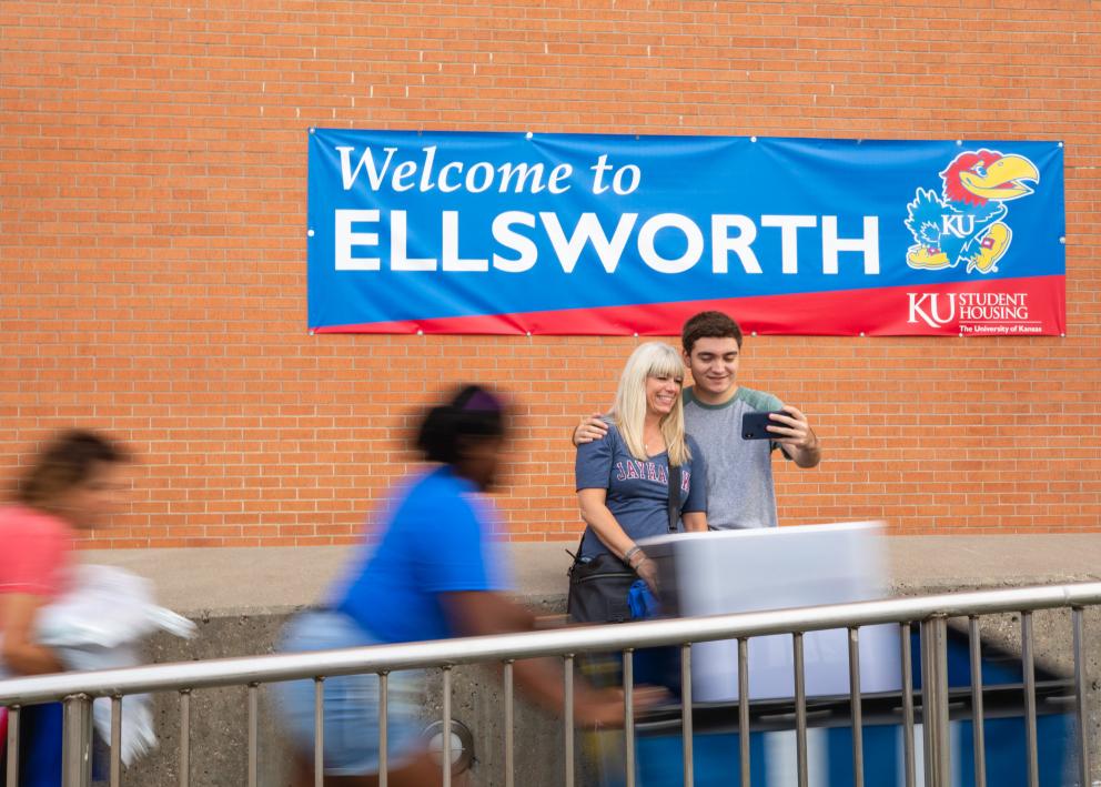a new student pausing to smile for a selfie with his mother on move-in day in front of the Ellsworth hall welcome banner