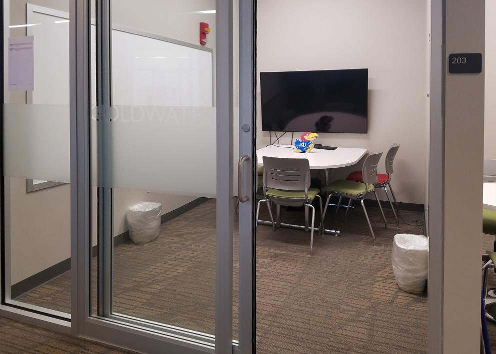 a small study room with a table and chairs, white board, TV, and sliding door