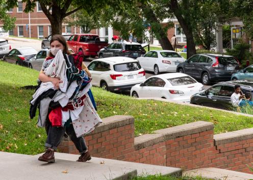 a student smiling under a face mask while carrying an armful of clothes up to their scholarship hall on move-in day
